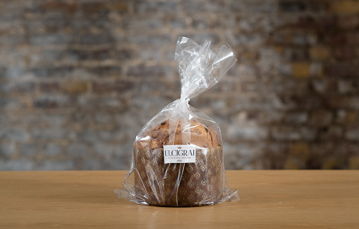A single delicious panettone sits on a wooden bench in front of an exposed brick wall